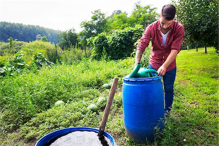 simsearch:6115-06732928,k - Young man filling watering can at barrel Stock Photo - Premium Royalty-Free, Code: 6115-08100806