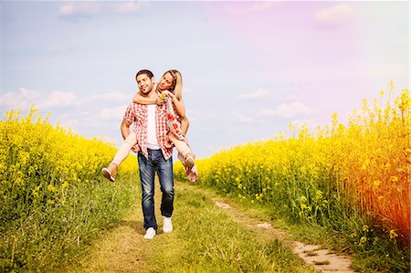 Young man carrying girlfriend piggyback along field path by colza field, Tuscany, Italy Stock Photo - Premium Royalty-Free, Code: 6115-08101051