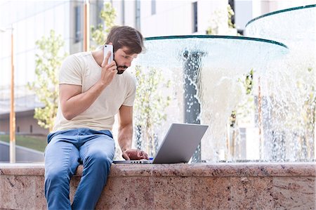 people on cell phones - Male university student using mobile phone and laptop Stock Photo - Premium Royalty-Free, Code: 6115-08101115