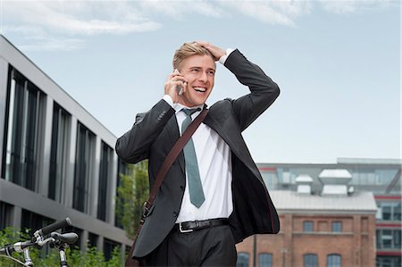 Happy young businessman using phone, Munich, Bavaria, Germany Stock Photo - Premium Royalty-Free, Code: 6115-08101374