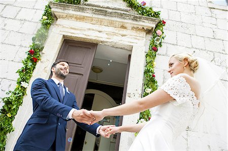 Bride and groom holding hands in front of chapel Stock Photo - Premium Royalty-Free, Code: 6115-08239389