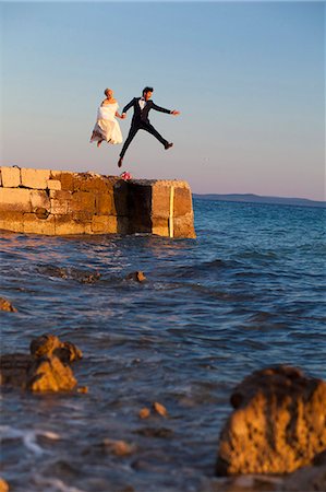 Bride and groom on pier jumping into the air Stock Photo - Premium Royalty-Free, Code: 6115-08239498