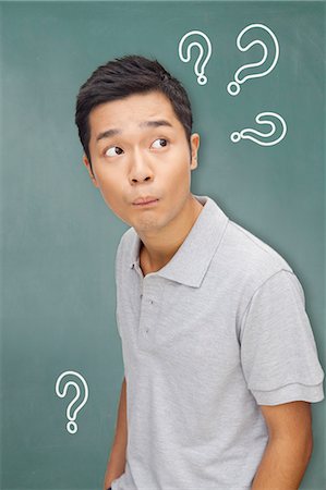 perplex - Portrait young man in front of blackboard with question marks Stock Photo - Premium Royalty-Free, Code: 6116-07085230