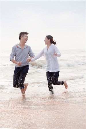 surf couple - Young couple holding hands and running by the waters edge on the beach, China Photographie de stock - Premium Libres de Droits, Code: 6116-07085920