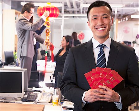 Businessman holding red envelopes and coworkers hanging decorations for Chinese new year Stock Photo - Premium Royalty-Free, Code: 6116-07086764