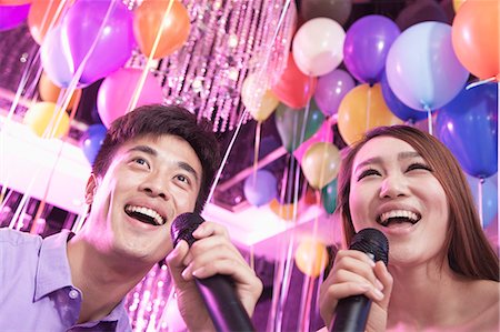 simsearch:6116-07236256,k - Two friends holding microphones and singing together at karaoke, balloons in the background Stock Photo - Premium Royalty-Free, Code: 6116-07236068