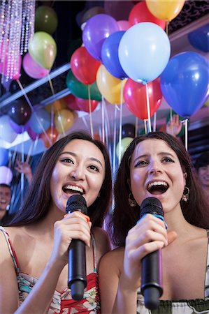 Two friends holding microphones and singing together at karaoke, balloons in the background Stock Photo - Premium Royalty-Free, Code: 6116-07236069