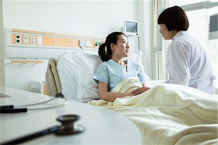 patient care - Female doctor sitting on hospital bed and discussing with young female patient Stock Photo - Premium Royalty-Free, Code: 6116-07236099