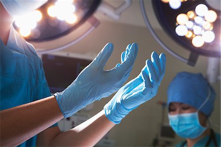 surgical gown - Midsection view of hands in surgical gloves and surgical lights in the operating room Photographie de stock - Premium Libres de Droits, Code: 6116-07236152