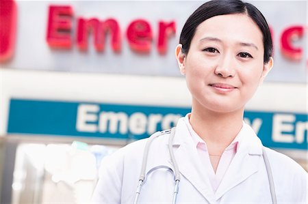 Portrait of smiling female doctor outside of the hospital, emergency room sign in the background Stock Photo - Premium Royalty-Free, Code: 6116-07236166