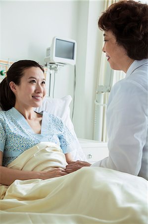 Female doctor sitting on hospital bed and discussing with young female patient Stock Photo - Premium Royalty-Free, Code: 6116-07236100