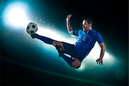 footballeur - Soccer player in mid air kicking the soccer ball, stadium lights at night in background Stock Photo - Premium Royalty-Free, Code: 6116-07236119