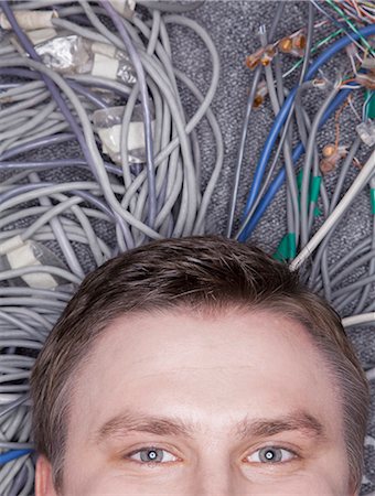 plugging in - Businessman's face lying down on computer cables looking up, half Stock Photo - Premium Royalty-Free, Code: 6116-07236259