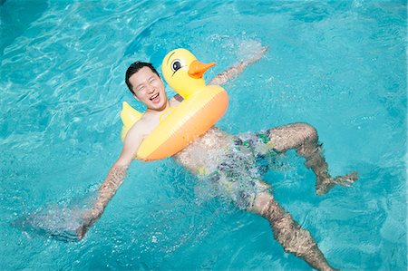simsearch:6116-07236315,k - Man wearing a yellow duck inflatable tube and playing in the pool Foto de stock - Sin royalties Premium, Código: 6116-07236327