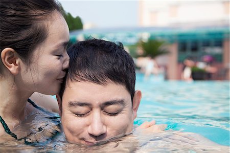simsearch:6116-07236315,k - Woman with eyes closed kissing man on the cheek in the water in the pool Foto de stock - Sin royalties Premium, Código: 6116-07236403