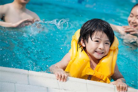 simsearch:6116-07236315,k - Portrait of smiling son in the water and holding onto the pools edge with family in the background Foto de stock - Sin royalties Premium, Código: 6116-07236405