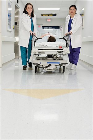 simsearch:693-06324311,k - Doctors pushing patient in bed through corridor Stock Photo - Premium Royalty-Free, Code: 6116-08915725