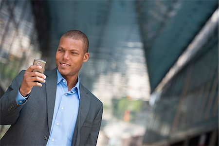 A Businessman In A Suit, With His Shirt Collar Unbuttoned. On A New York City Street. Using A Smart Phone. Stock Photo - Premium Royalty-Free, Code: 6118-07121964