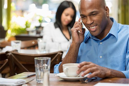 Business People. Two People Sitting At Coffee Shop Tables, Checking Their Messages. Stock Photo - Premium Royalty-Free, Code: 6118-07122000