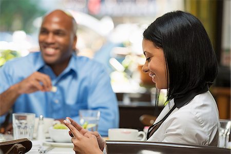 simsearch:6118-07203820,k - Business People. A Woman Checking Her Phone, At A Coffeeshop Table. A Man At Another Table. Stock Photo - Premium Royalty-Free, Code: 6118-07122005