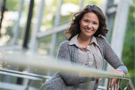 Business People Outdoors. A Businesswoman In A Light Grey Jacket, Leaning On A Railing Smiling. Relaxing. Stock Photo - Premium Royalty-Free, Code: 6118-07122037