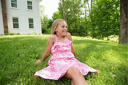 simsearch:6118-07122184,k - A Young Girl In A Pink Patterned Sundress Sitting On The Grass Under The Trees In A Farmhouse Garden. Stock Photo - Premium Royalty-Free, Code: 6118-07122167