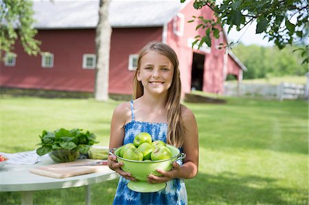 simsearch:6118-07122193,k - Family Party. A Young Girl With Long Blonde Hair Wearing A Blue Sundress, Carrying A Large Bowl Of Crisp Green Skinned Apples. Foto de stock - Sin royalties Premium, Código: 6118-07122176