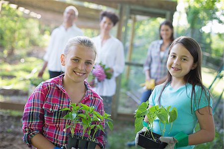 simsearch:6118-07122184,k - Organic Farm. Summer Party. Two Girls Sitting Holding Young Plants, With A Mature Couple And A Young Woman Looking On. Stock Photo - Premium Royalty-Free, Code: 6118-07122136