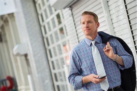 A Man With His Jacket Slung Over His Shoulder, Checking His Phone. Stock Photo - Premium Royalty-Free, Code: 6118-07122447