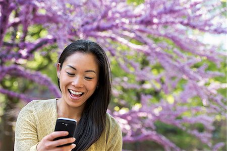 park attire - A Woman Sitting In A Park Looking At Her Smart Phone And Laughing. Stock Photo - Premium Royalty-Free, Code: 6118-07122470