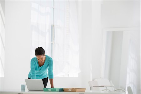 Business. A Woman Leaning Over A Desk Using A Laptop Computer. Photographie de stock - Premium Libres de Droits, Code: 6118-07122592