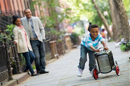 family city - A Young Boy Playing With A Old Fashioned Toy Car On Wheels On A City Street. A Couple Looking On. Stock Photo - Premium Royalty-Free, Code: 6118-07122533