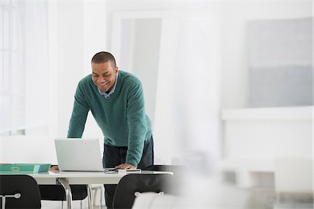 ethnicity - Business. A Man Standing Over A Desk, Leaning Down To Use A Laptop Computer. Stock Photo - Premium Royalty-Free, Code: 6118-07122539