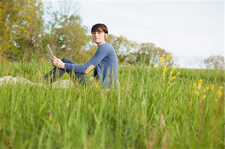 simsearch:6118-07122740,k - A Young Woman Sitting In An Open Space, A Grass Field, On A Blanket, Holding A Digital Tablet. Photographie de stock - Premium Libres de Droits, Code: 6118-07122743