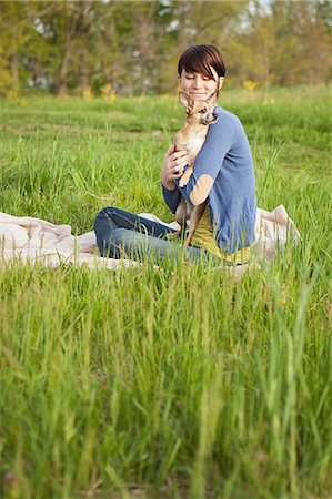 simsearch:6118-07122740,k - A Young Woman Sitting In A Field, On A Blanket, Holding A Small Chihuahua Dog. Photographie de stock - Premium Libres de Droits, Code: 6118-07122744