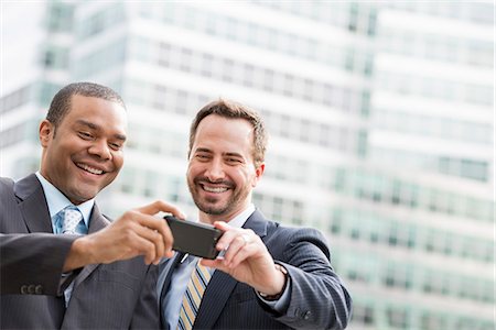 simsearch:6118-07440408,k - City. Two Men In Business Suits, Looking At A Smart Phone, Smiling. Stock Photo - Premium Royalty-Free, Code: 6118-07122833