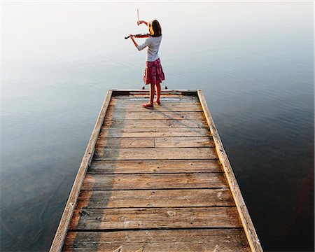 A ten year old girl playing the violin at dawn on a wooden dock. Stock Photo - Premium Royalty-Free, Code: 6118-07203253
