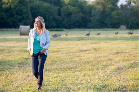 A woman walking across a field, away from a flock of geese outdoors in the fresh air. Stock Photo - Premium Royalty-Free, Code: 6118-07203410