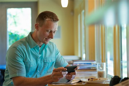 simsearch:6118-07203820,k - A man with short cropped hair sitting at a cafe table, using a smart phone. Stock Photo - Premium Royalty-Free, Code: 6118-07203570