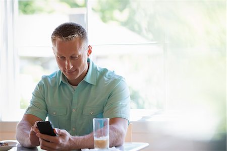simsearch:6118-07203820,k - A man with short cropped hair sitting at a cafe table, using a smart phone. Stock Photo - Premium Royalty-Free, Code: 6118-07203575