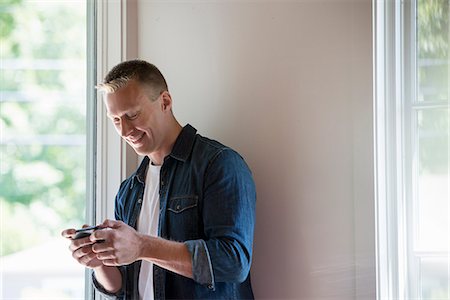 simsearch:6118-07203820,k - A man standing in a quiet corner of a cafe, using a smart phone. Stock Photo - Premium Royalty-Free, Code: 6118-07203580