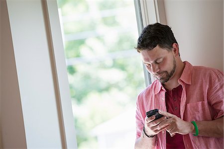 simsearch:6118-07203820,k - A man standing in a quiet corner of a cafe, using a smart phone. Stock Photo - Premium Royalty-Free, Code: 6118-07203581