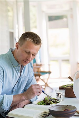 A man seated at a cafe table eating a salad and reading a book. Foto de stock - Sin royalties Premium, Código: 6118-07203599