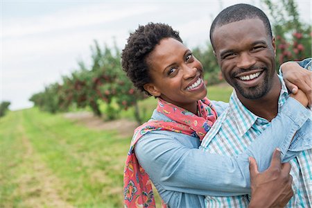 simsearch:6118-07203696,k - An organic apple tree orchard. A couple hugging and smiling at the camera. Stock Photo - Premium Royalty-Free, Code: 6118-07203695