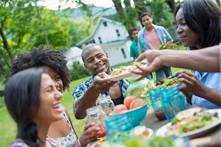 A group of adults and young people at a meal in the garden of a farmhouse. Passing plates and raising glasses. Stock Photo - Premium Royalty-Free, Code: 6118-07203743