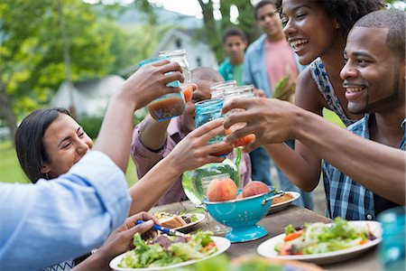 side table - A group of adults and young people at a meal in the garden of a farmhouse. Passing plates and raising glasses. Foto de stock - Sin royalties Premium, Código: 6118-07203747