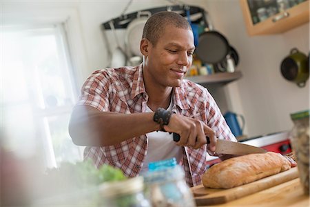 simsearch:6118-07203820,k - A man in a kitchen slicing a loaf of bread. Stock Photo - Premium Royalty-Free, Code: 6118-07203798