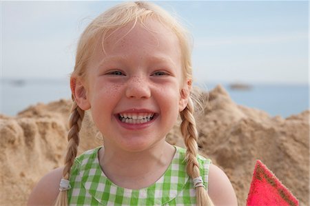 pigtail braid - A girl beside a huge pile of sand on the beach, grinning at the camera. Stock Photo - Premium Royalty-Free, Code: 6118-07203847