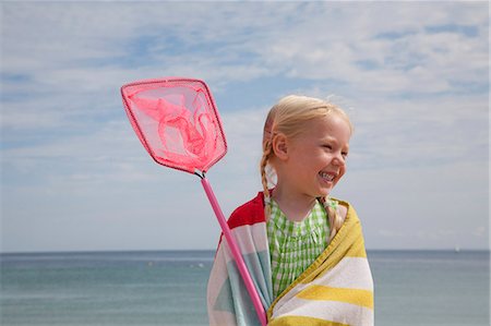 A young girl with a beach towel around her shoulders, carrying a small fishing net. Stock Photo - Premium Royalty-Free, Code: 6118-07203853