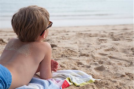 sand sea kids - A boy lying on his front on the sand looking out to sea. Photographie de stock - Premium Libres de Droits, Code: 6118-07203850